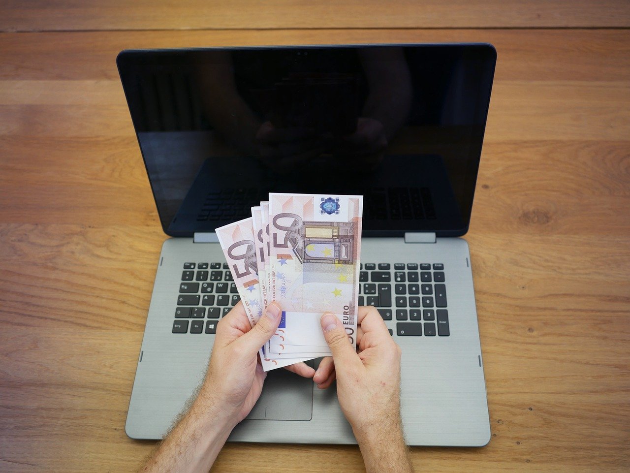 A person's hand holding money in front of the laptop